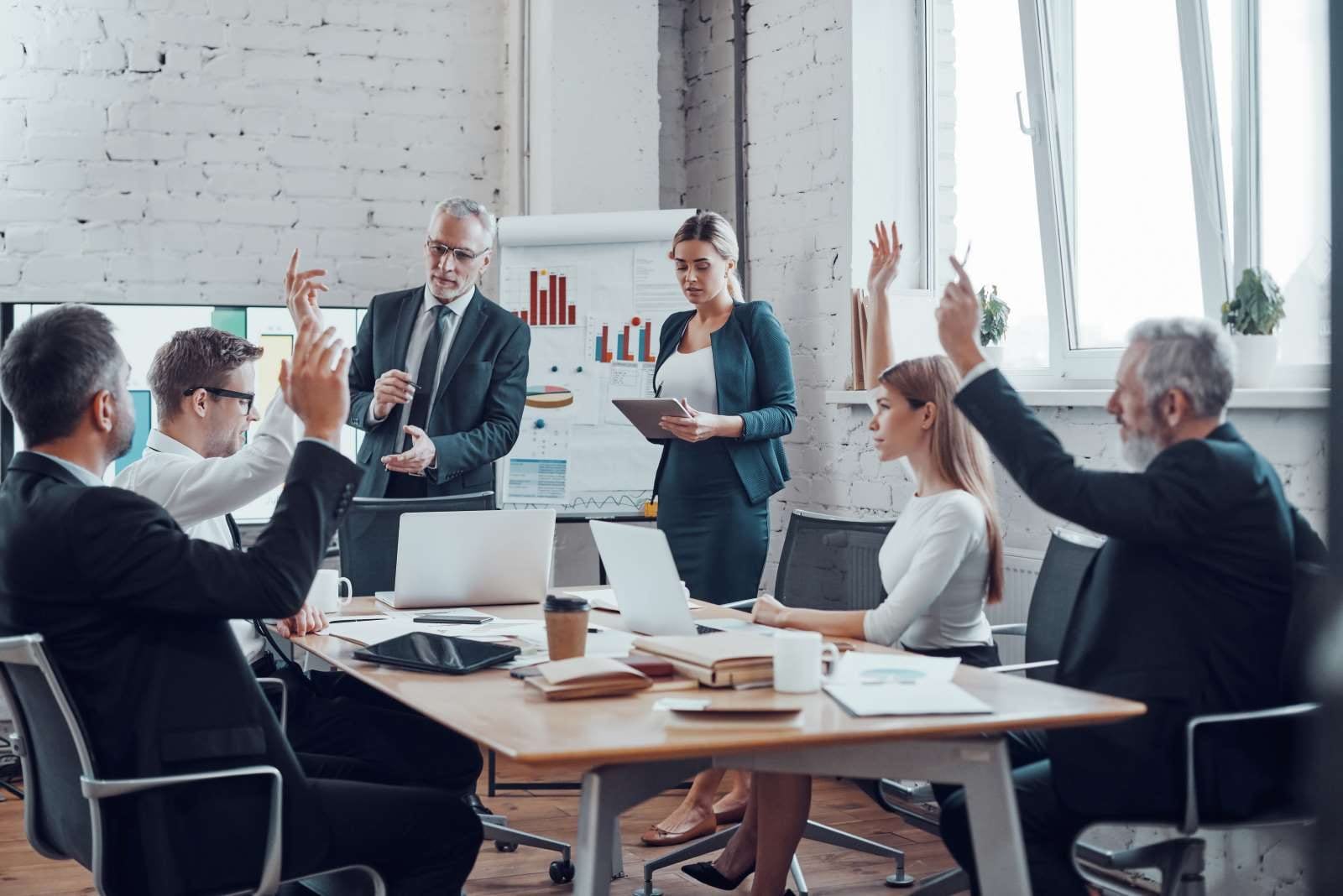 people with hands up in small meeting