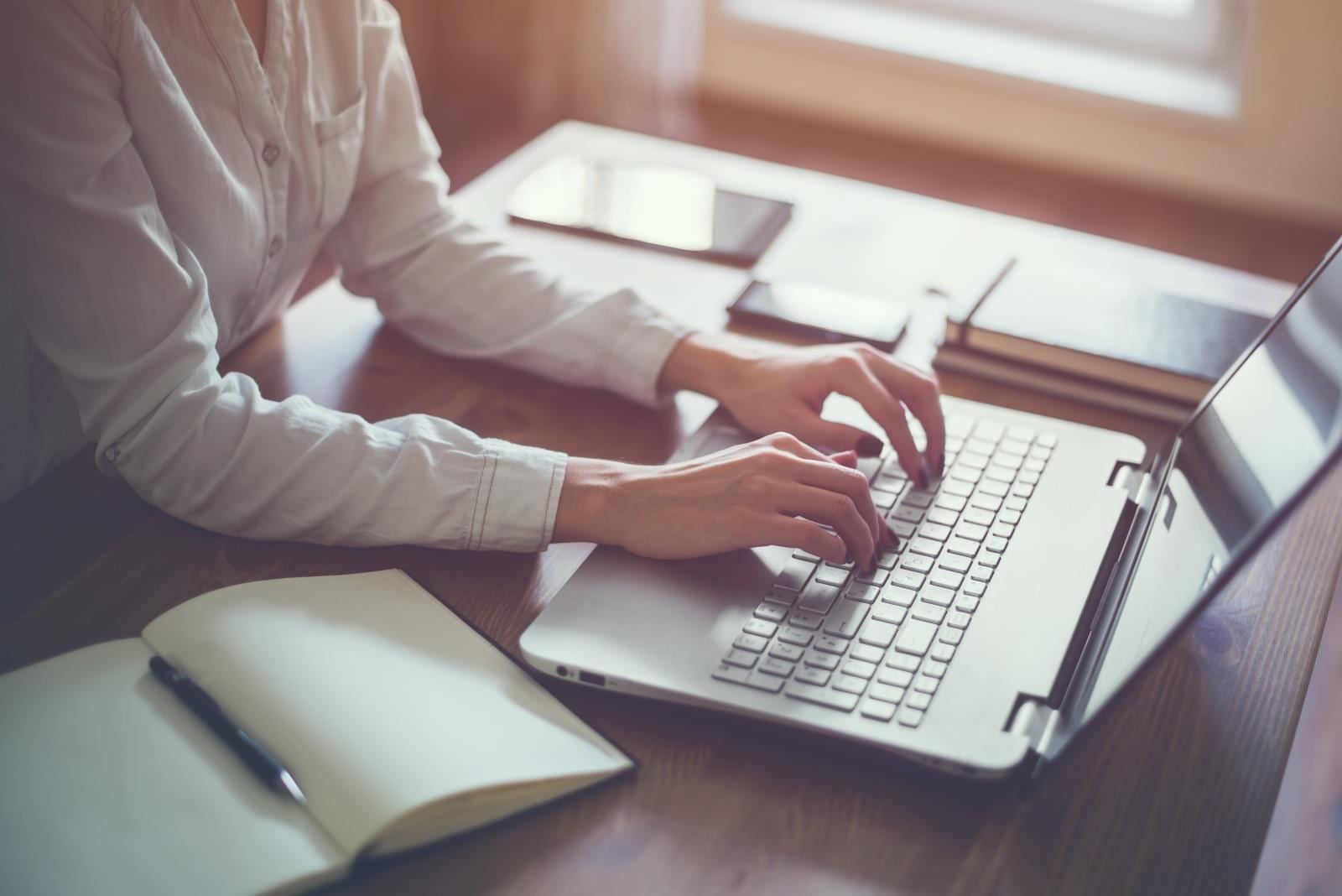 woman typing on laptop with notebook